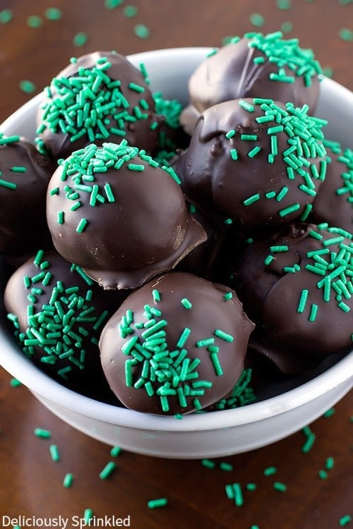 A white bowl is filled with green sprinkled mint oreo truffles.