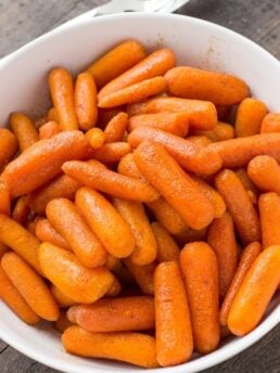 Instant Pot Glazed Carrots in white bowl with a spoon on the table behind it.