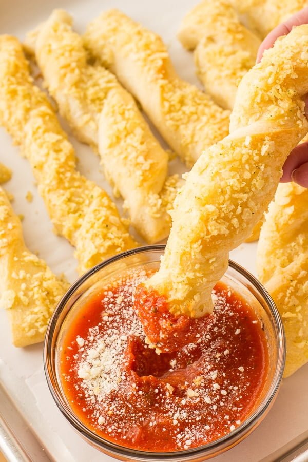 A breadstick is being dunked into a small cup of marinara sauce.