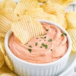 An up-close shot of a cup of potato chip dip surrounded with potato chips.