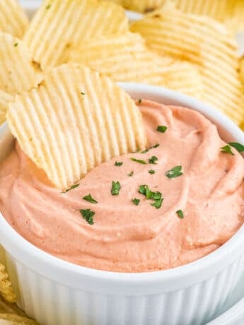An up-close shot of a cup of potato chip dip surrounded with potato chips.