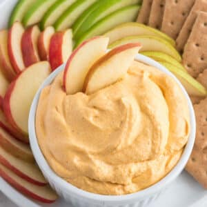 A bowl of pumpkin dip with apples and graham crackers around the bowl.