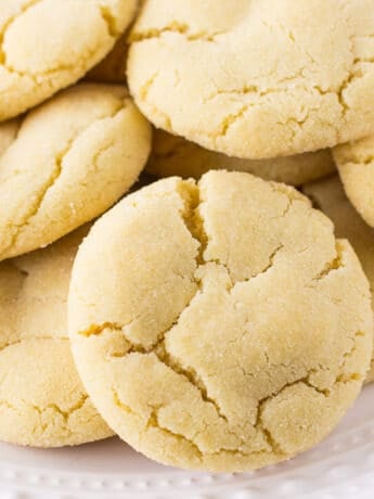 A closeup of a pile of sugar cookies on a white plate.