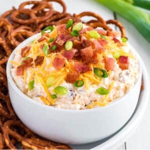 Bowl of pretzel dip surrounded by pretzels and topped with more cheese and bacon.