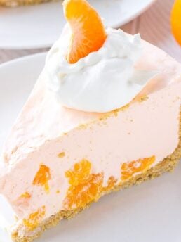 A piece of creamy orange pie on a plate topped with whipped cream and a mandarin orange.