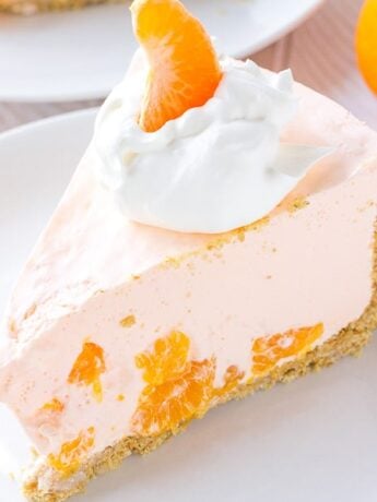 A piece of creamy orange pie on a plate topped with whipped cream and a mandarin orange.