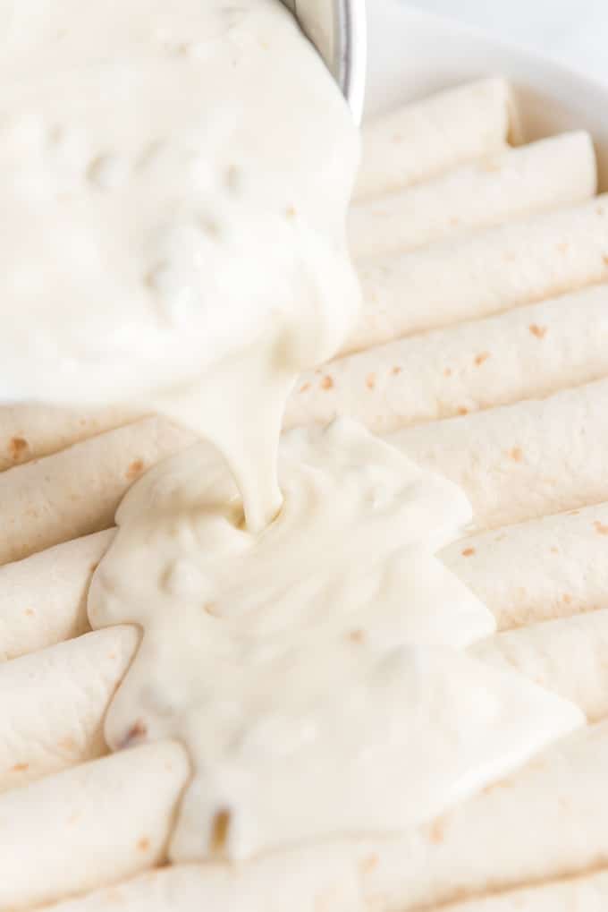 pouring white sauce on easy chicken enchiladas