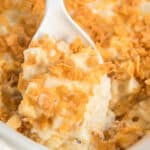 Cheesy hash brown casserole with corn flakes in a dish with a spoon scooping some out.
