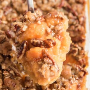 A spoonful of old fashioned sweet potato casserole held up over the full baking dish.