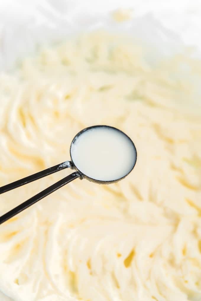 A tablespoon of milk is being added to the creamed frosting mixture. 