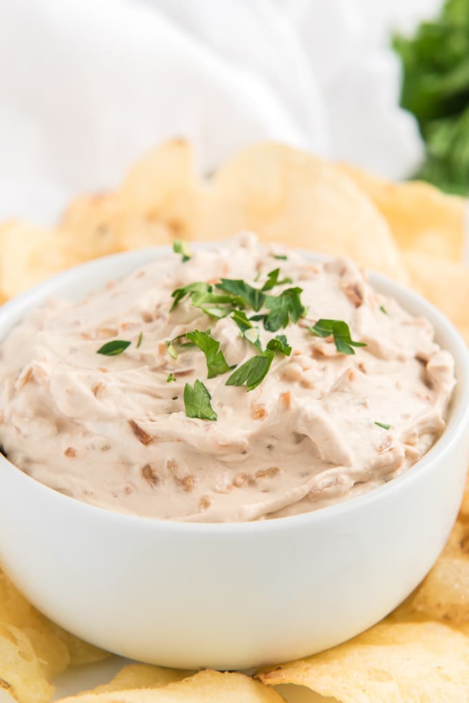 A bowl of French onion dip is placed next to potato chips, ready to be eaten.