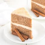 two-layer cinnamon cake topped with cinnamon buttercream frosting sliced on a plate.