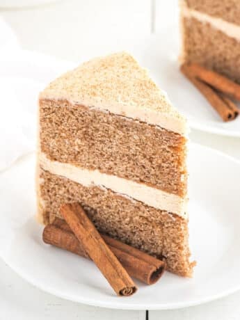two-layer cinnamon cake topped with cinnamon buttercream frosting sliced on a plate.