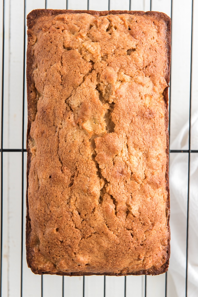 A loaf of apple bread is presented on a wire cooling rack. 