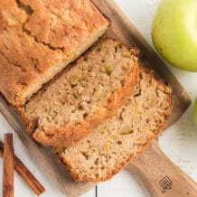 slices of apple bread are presented on a wooden cutting board next to the loaf.