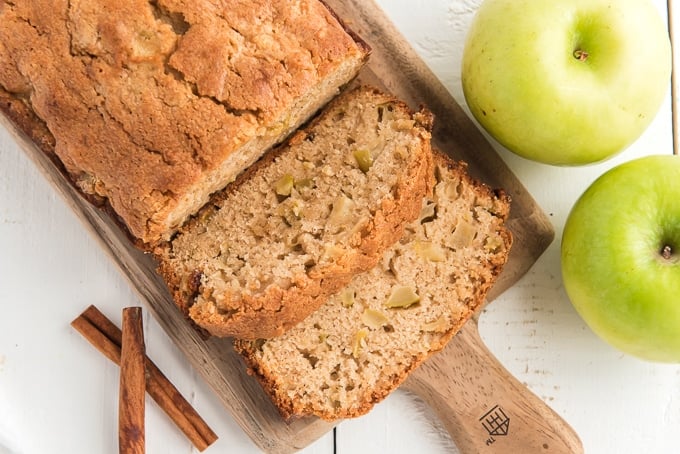 slices of apple bread are presented on a wooden cutting board next to the loaf.