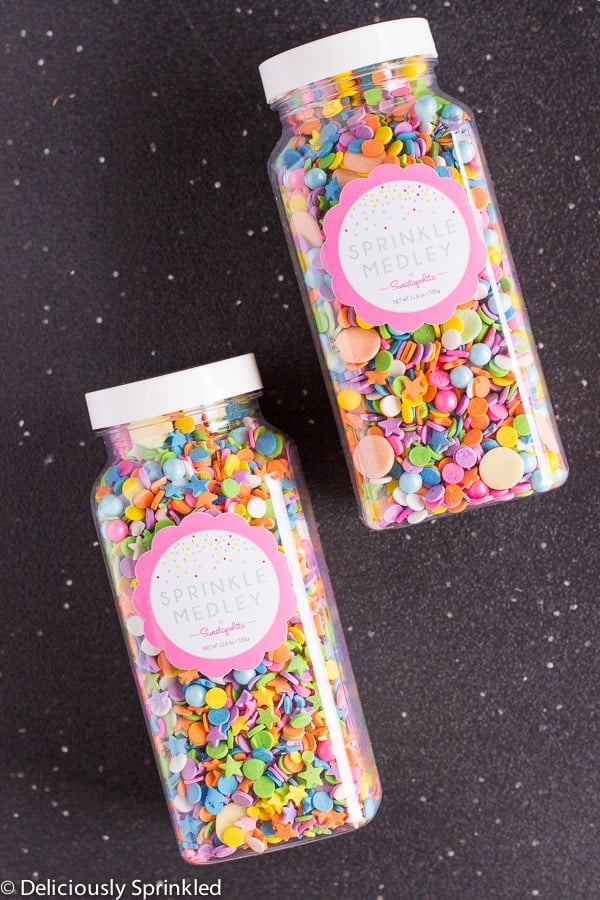 Two containers of sprinkles are placed on a black surface.