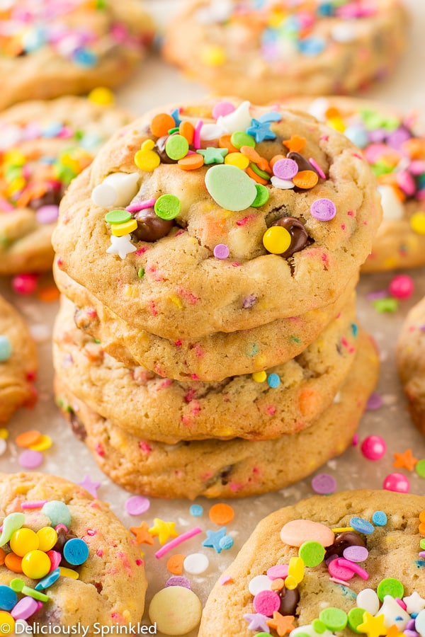 A stack of cooked birthday cake cookies is presented on a white surface with more cookies.