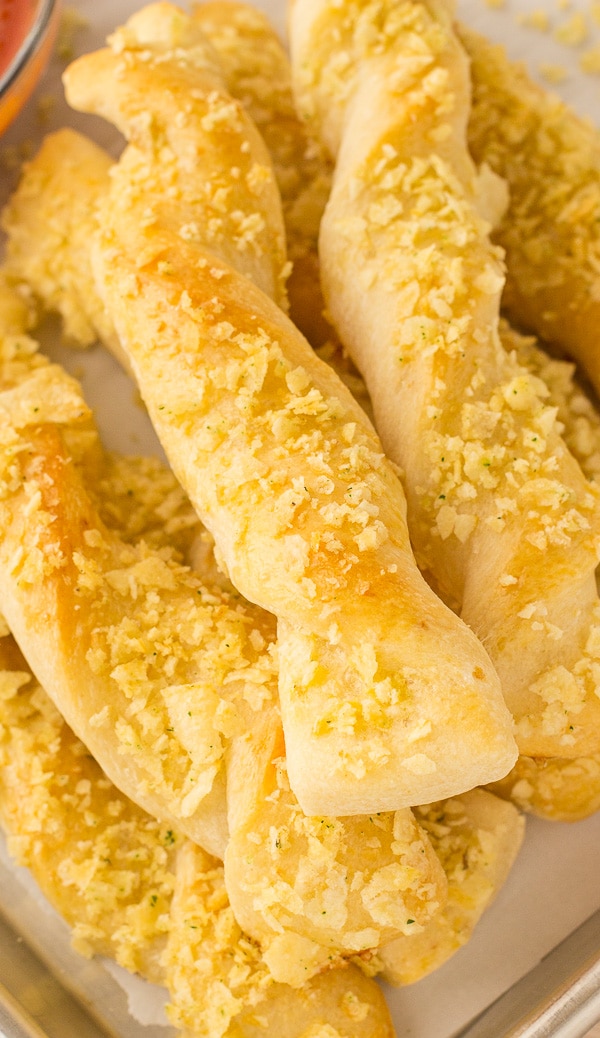 A stack of baked breadsticks is topped with golden crushed potato chips.