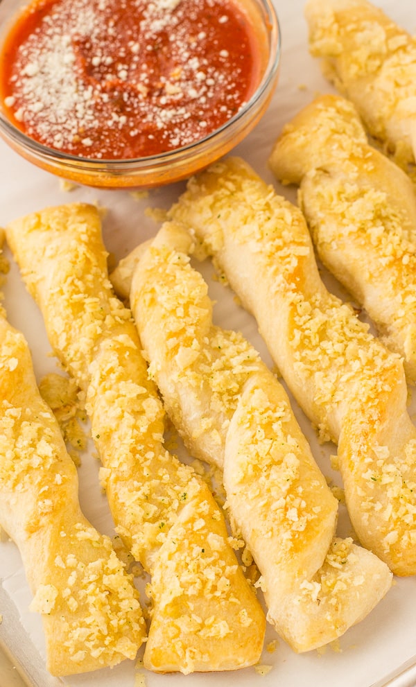 A row of freshly baked breadsticks is presented next to a cup of red sauce.