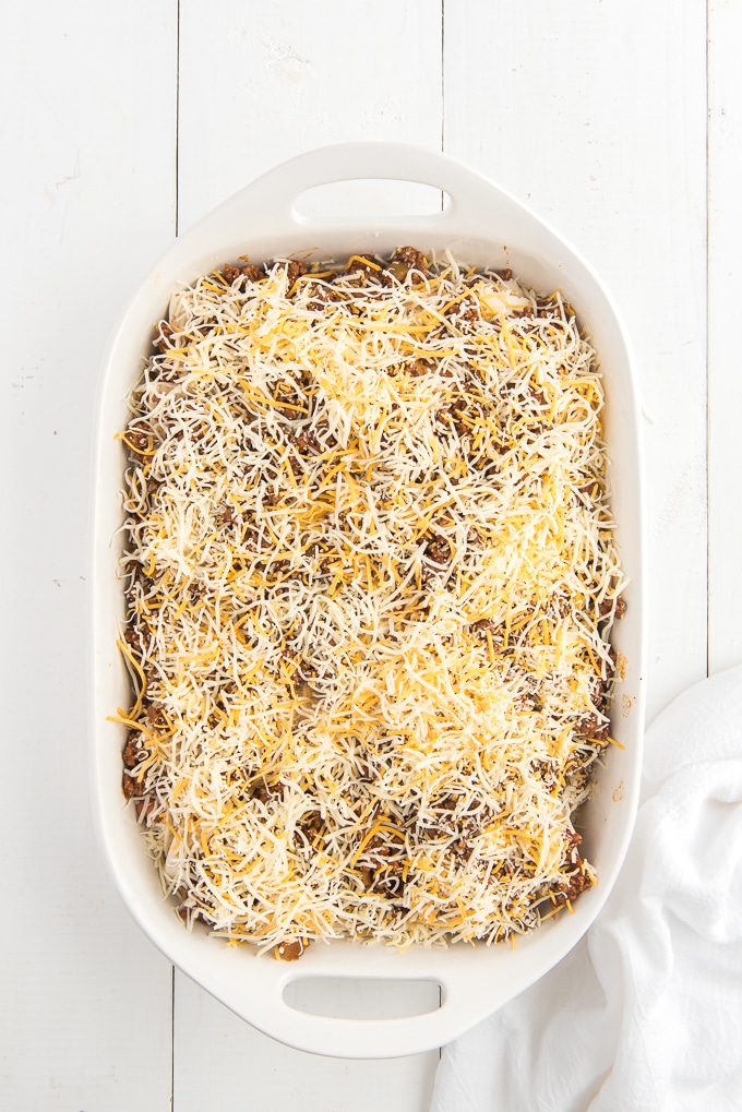 Cheese is placed on top of an uncooked lasagna in a white casserole dish.