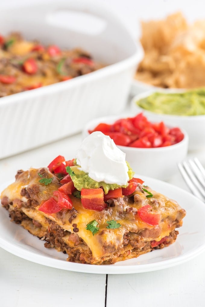 A serving of Mexican lasagna has been plated and topped with tomatoes and sour cream.