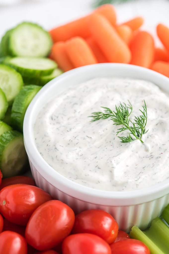 Dill dip and veggies are presented on a white surface. 