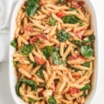 Pasta is stirred with baby spinach in a white baking dish.