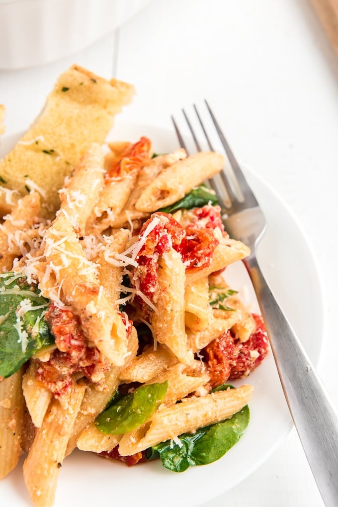 Penne noodles are tossed in baked feta cheese and tomatoes on a plate. 