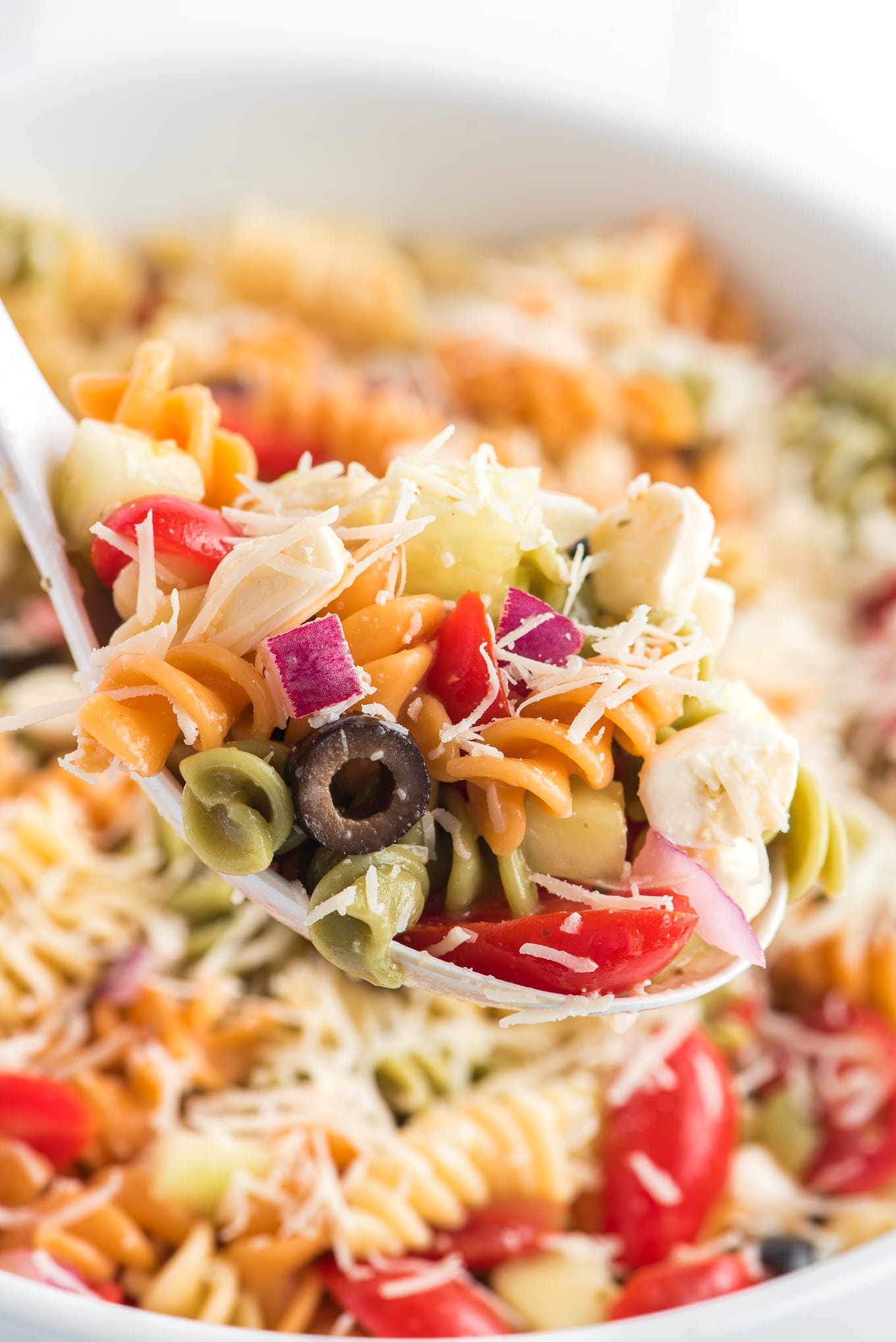 Pasta salad served on a spoon/ Easy Pasta Salad is the best cold pasta salad with tri color pasta, tomatoes, cucumbers, onions, and mozzarella cheese tossed in olive garden Italian dressing. 