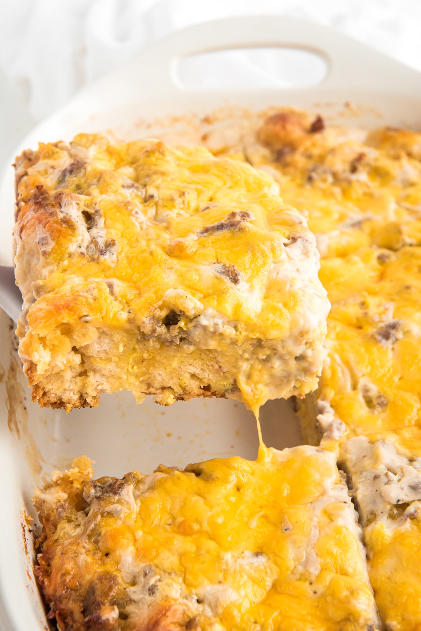 A spatula lifting out a square of easy breakfast casserole from the pan to serve.