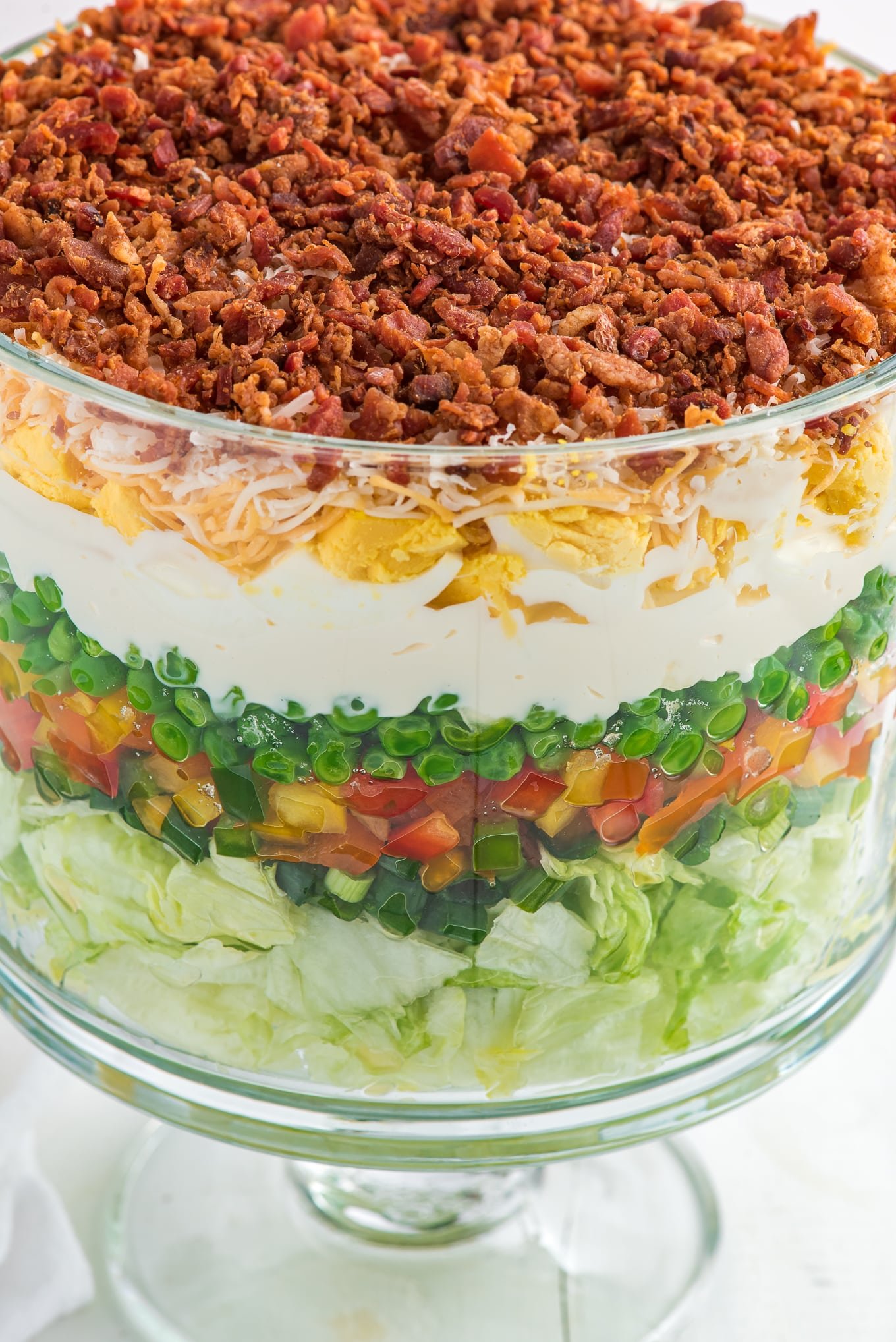 Trifle bowl filled with seven layer salad focused in on bacon on the top.