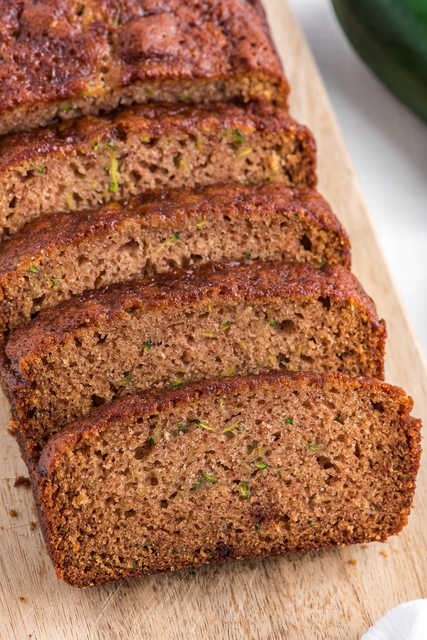 sliced zucchini bread on a wood cutting board. / This zucchini bread is a quick bread recipe that is made with grated zucchini, flour, sugar, eggs, applesauce, orange juice, and cinnamon. It has a moist and tender texture with a slightly sweet flavor perfect for breakfast or even a healthier dessert.