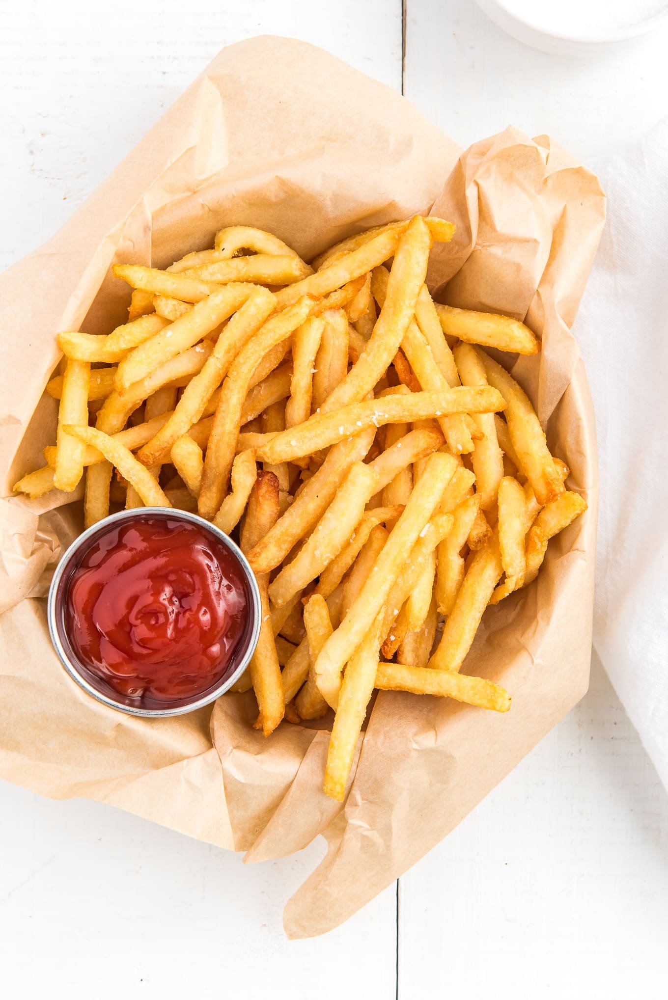 air fryer frozen french fries in a basket with a side of ketchup. / Enjoy crispy and delicious frozen French fries in minutes with this easy air fryer recipe. Get that classic crispy texture and savory flavor you love, with the convenience of the air fryer.