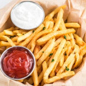 air fryer frozen french fries in a basket with a side of ketchup and ranch dressing. /Enjoy crispy and delicious frozen French fries in minutes with this easy air fryer recipe. Get that classic crispy texture and savory flavor you love, with the convenience of the air fryer.
