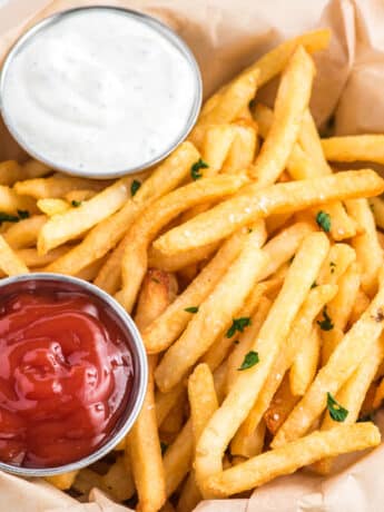 air fryer frozen french fries in a basket with a side of ketchup and ranch dressing. /Enjoy crispy and delicious frozen French fries in minutes with this easy air fryer recipe. Get that classic crispy texture and savory flavor you love, with the convenience of the air fryer.