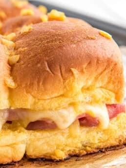 Hawaiian Rolls Sliders with ham and Swiss cheese on baking tray./ Delicious ham and cheese sliders on soft and sweet Hawaiian rolls, stacked with melted cheese, juicy ham, and topped with a golden-brown glaze, perfect for a quick dinner or appetizer.