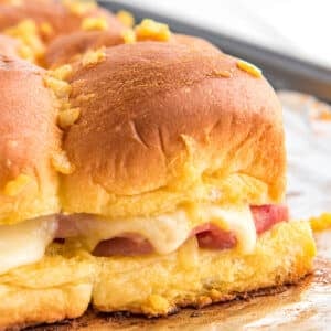 Hawaiian Rolls Sliders with ham and Swiss cheese on baking tray./ Delicious ham and cheese sliders on soft and sweet Hawaiian rolls, stacked with melted cheese, juicy ham, and topped with a golden-brown glaze, perfect for a quick dinner or appetizer.