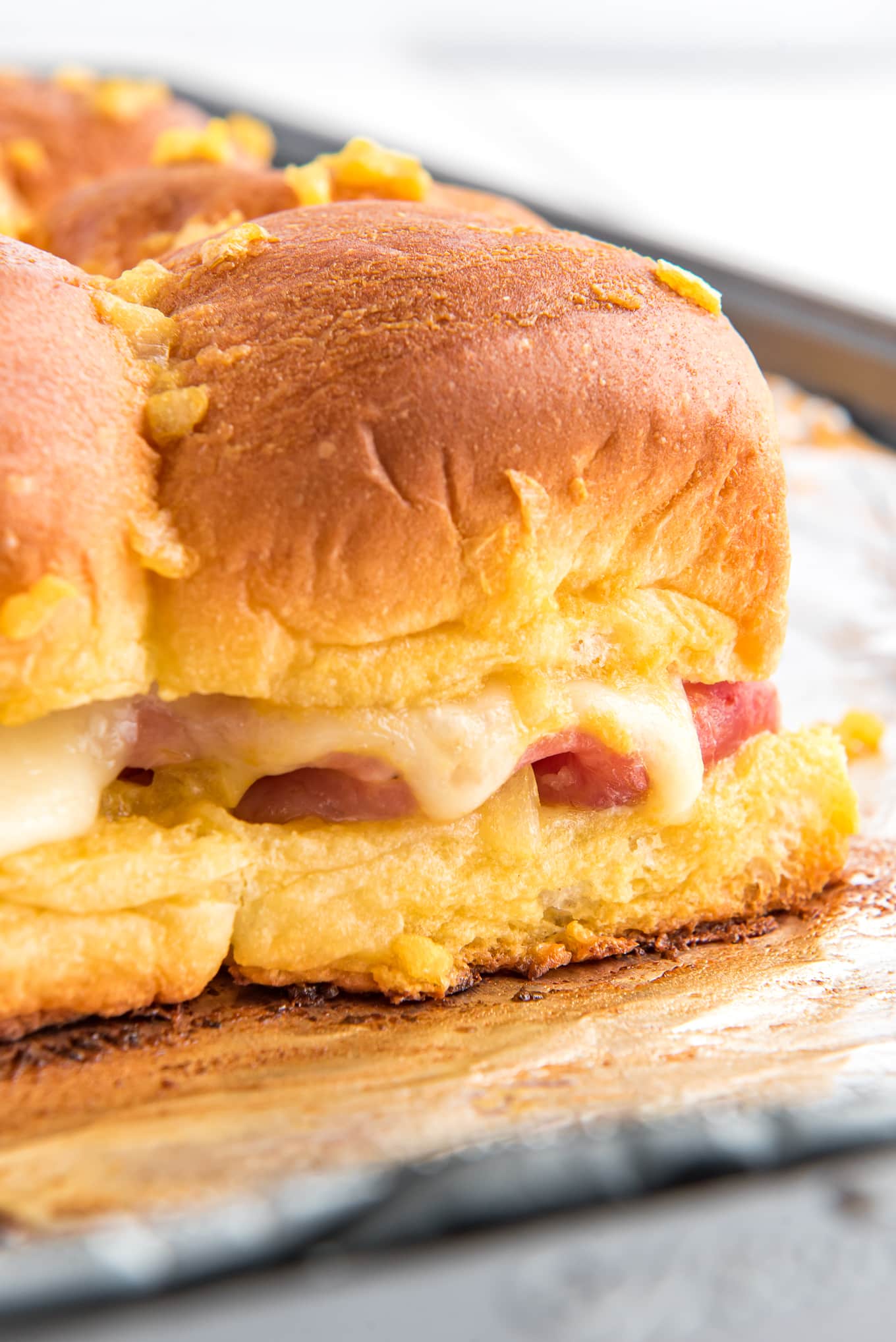 Hawaiian Rolls Sliders with ham and Swiss cheese on baking tray./ Delicious ham and cheese sliders on soft and sweet Hawaiian rolls, stacked with melted cheese, juicy ham, and topped with a golden-brown glaze, perfect for a quick dinner or appetizer. 