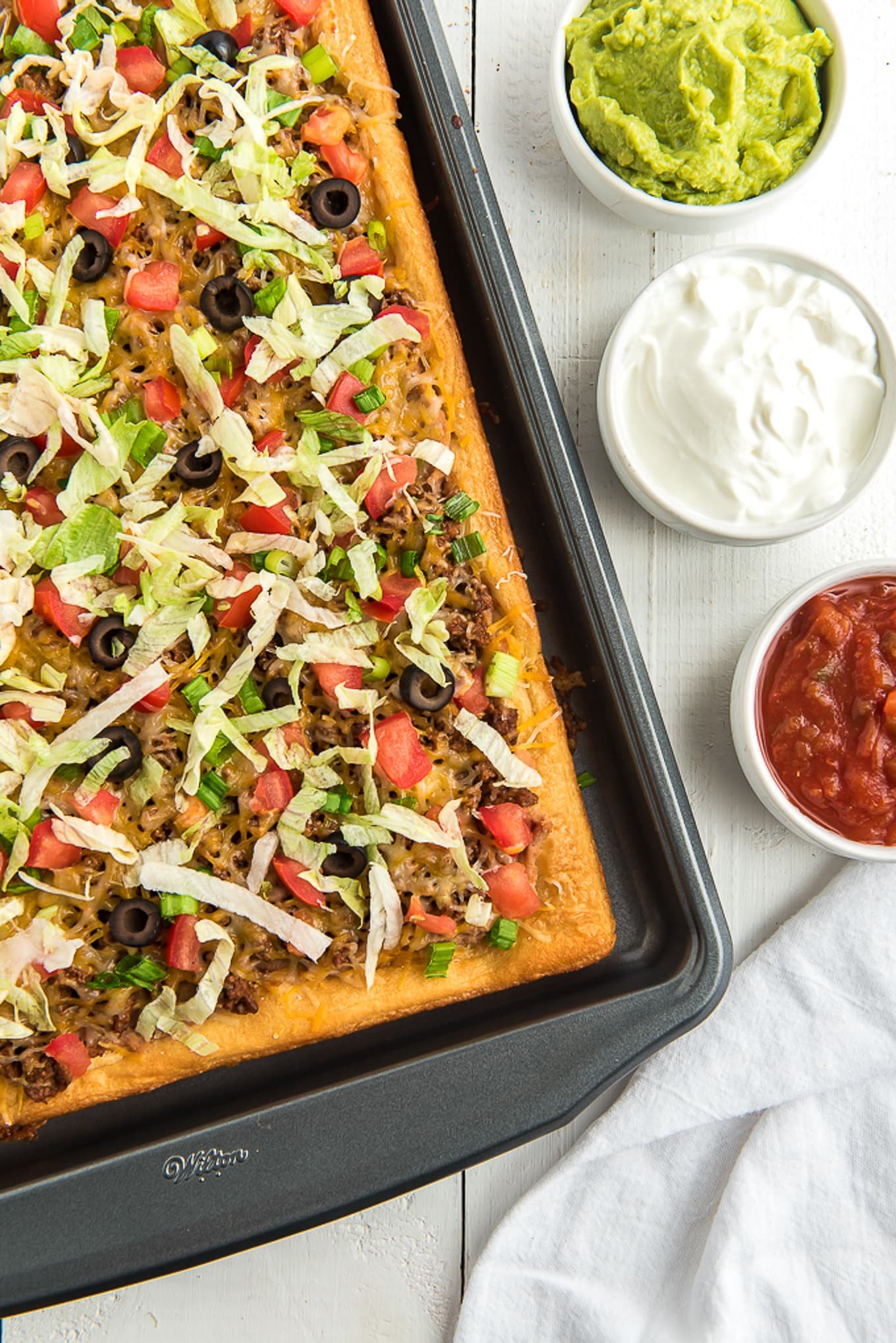taco pizza recipe on sheet pan topped with lettuce, lettuce, tomatoes and olives./ 