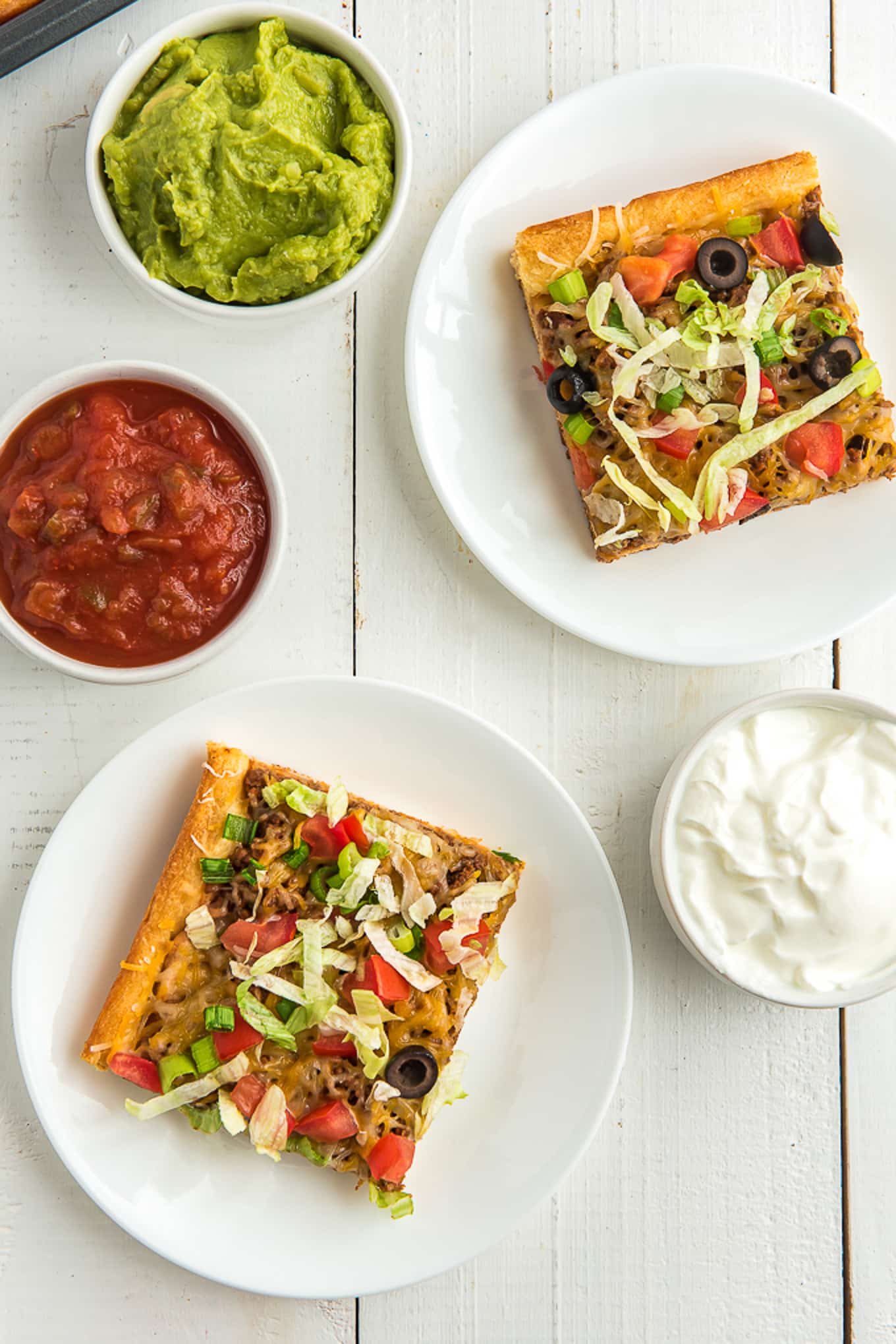 two slices of taco pizza on a plate with salsa, guacamole on the side. /