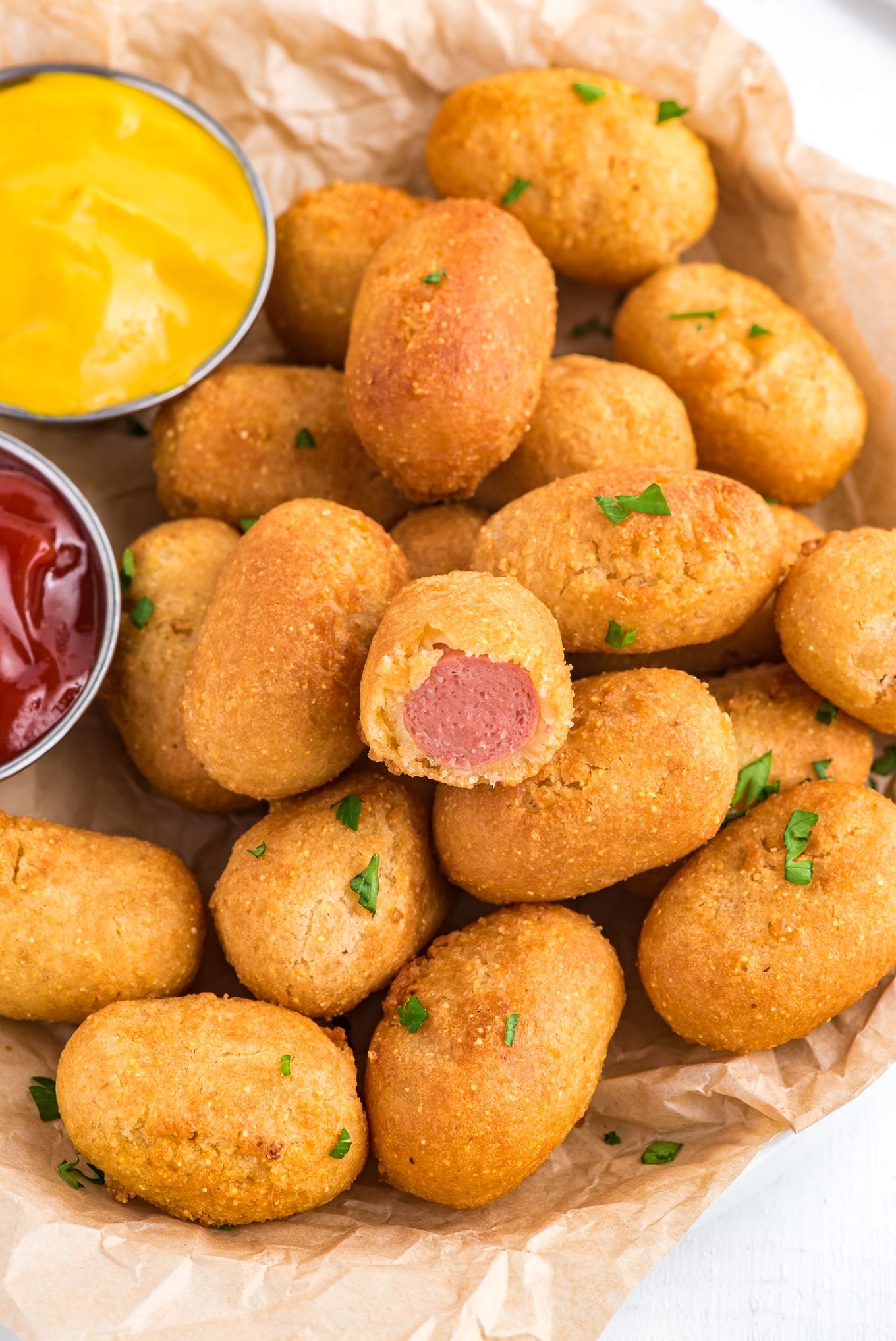 mini corn dogs in a basket with ketchup and mustard on the side. 