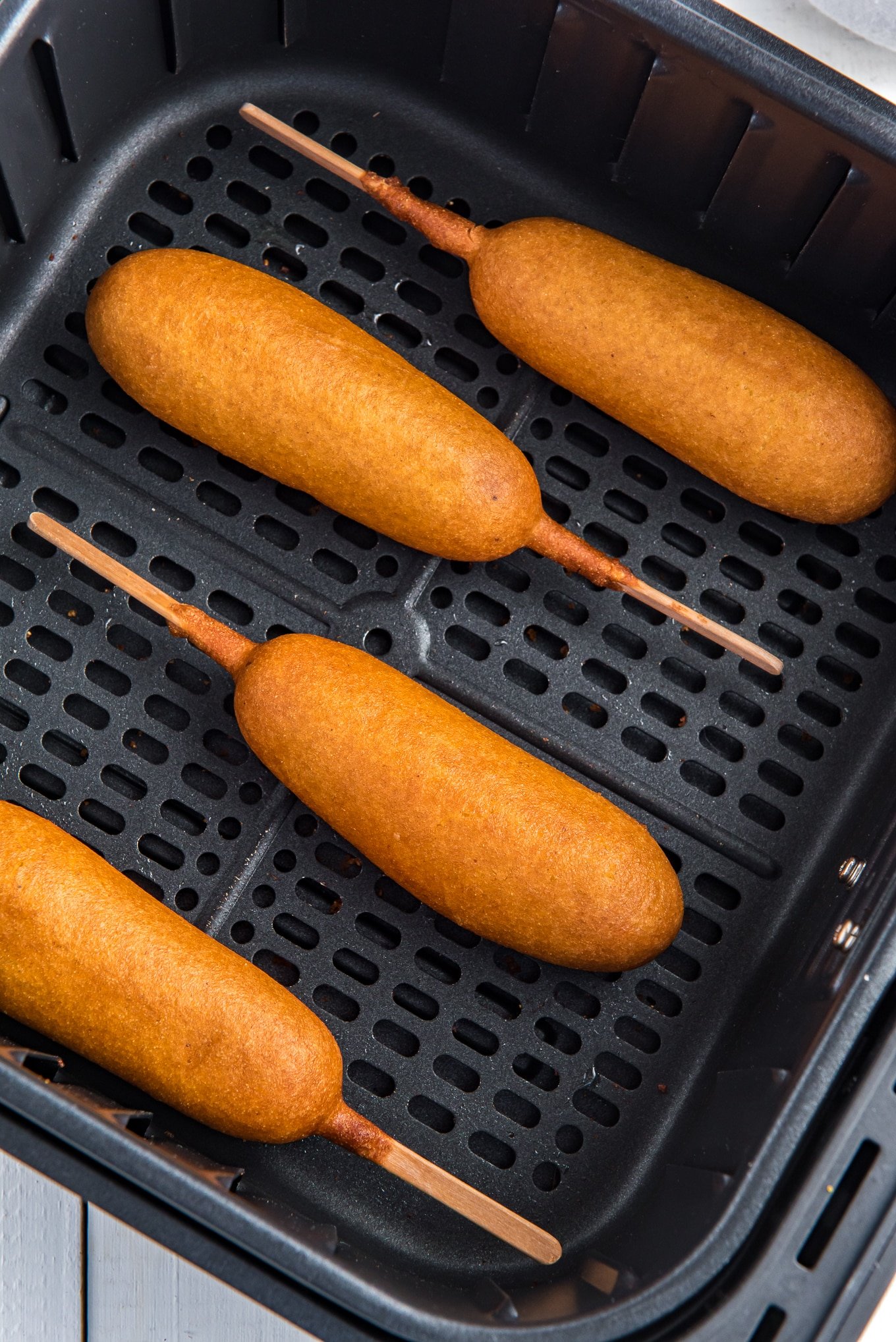A close-up photo of four corn dogs in an air fryer basket.