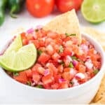 Pico de gallo in a bowl with lime slices and chips.