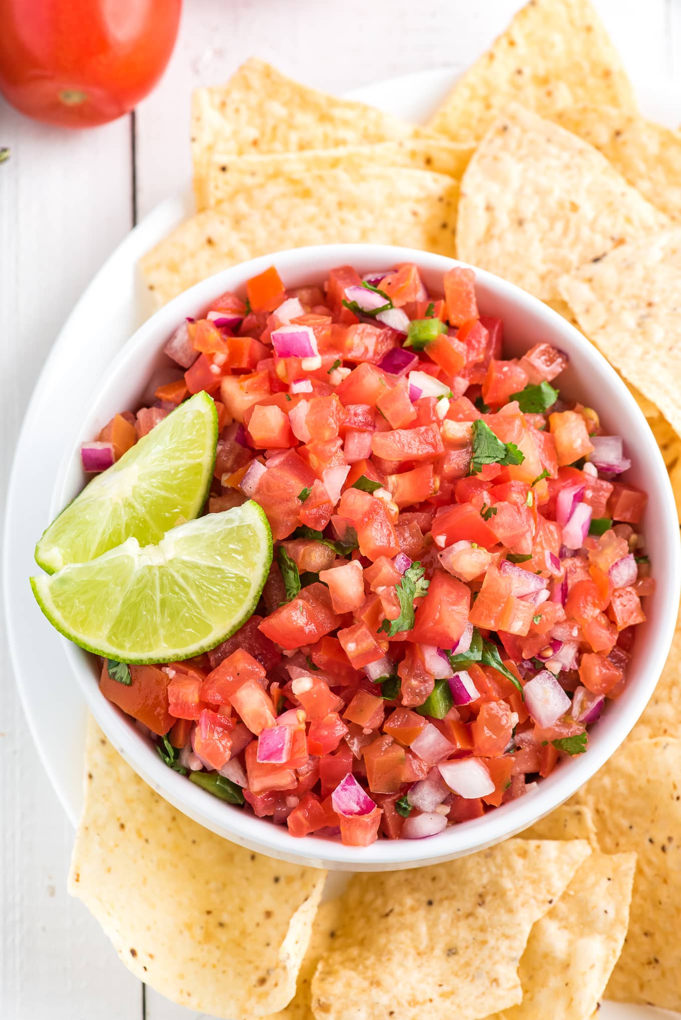An overhead shot of pico de gallo in a bowl surrounded by tortilla chips on a plate.