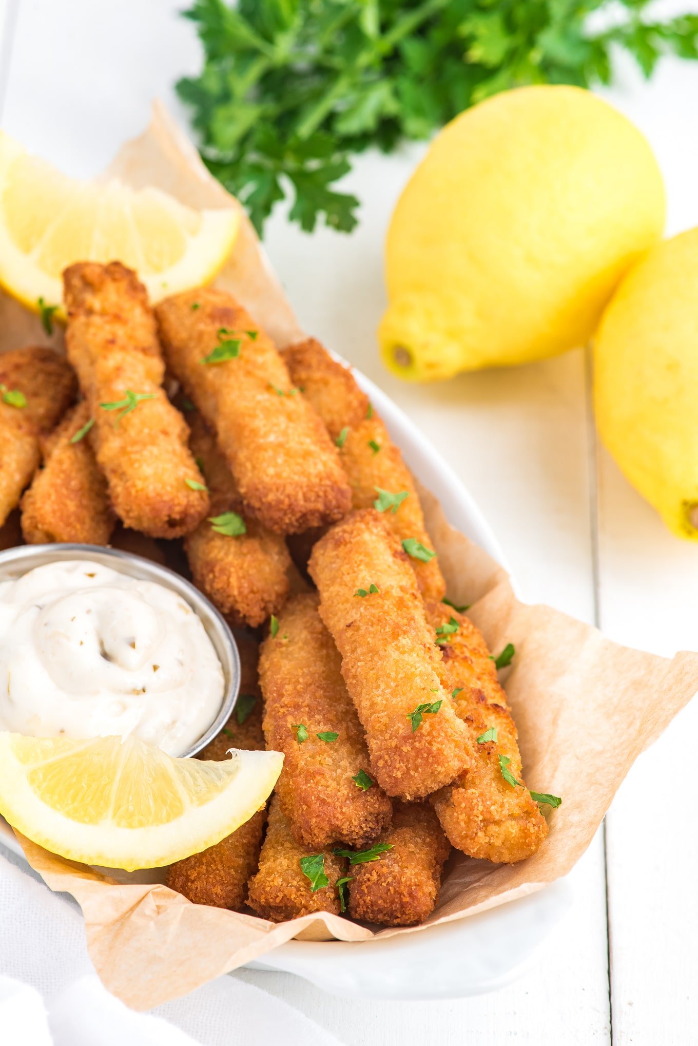 A basket of fish sticks in air fryer with lemon wedge and tartar sauce and lemons in the background.