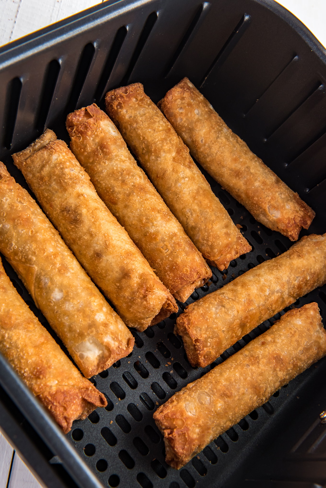 Egg rolls at the bottom of an air fryer basket cooked to a delicious crispy golden brown outside texture. 