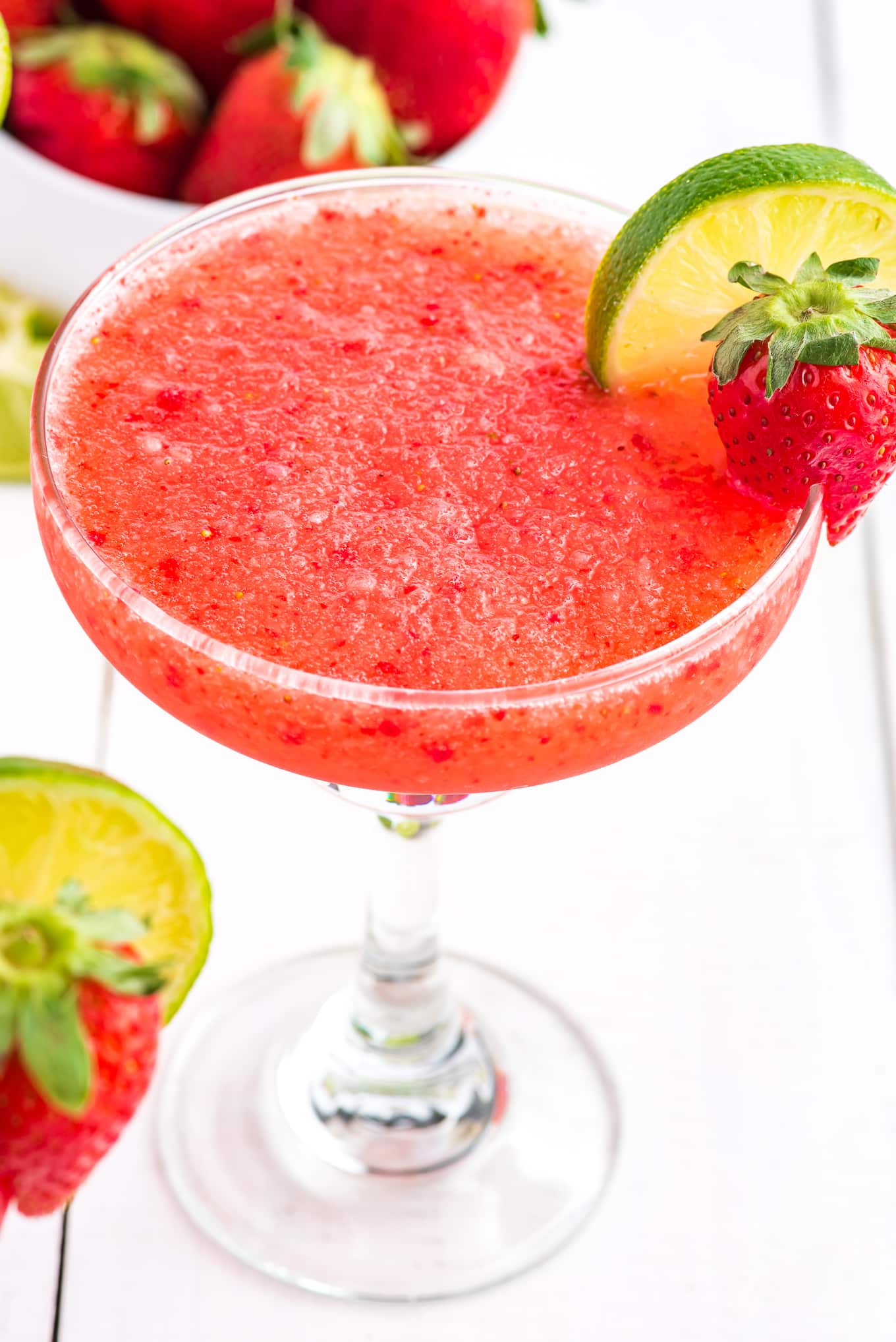 A round stemmed margarita glass with frozen strawberry margarita and garnished with strawberry and lime.