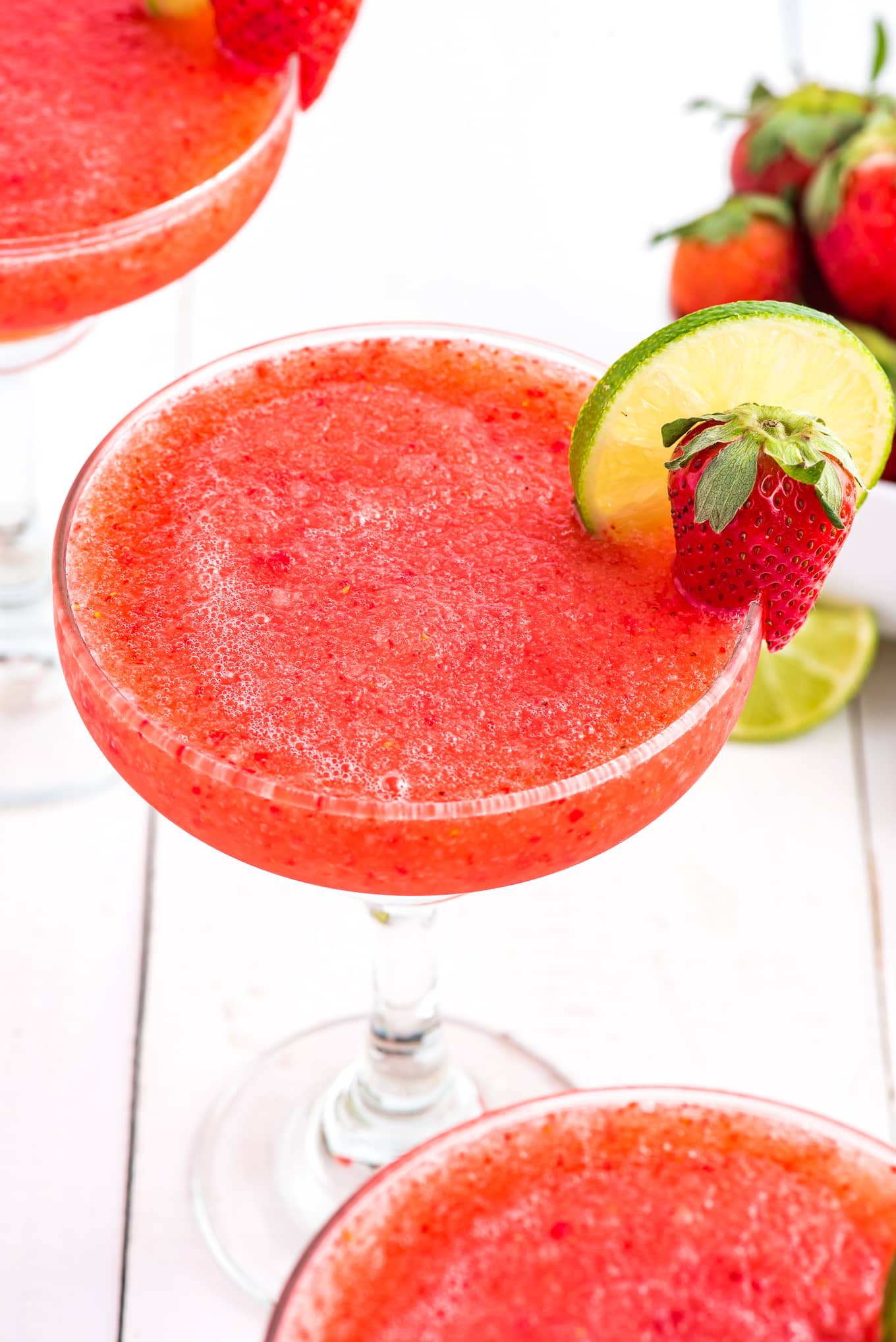 A frozen strawberry margarita in a glass with a small strawberry and lime round.