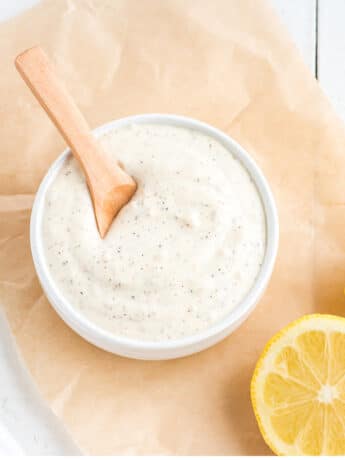 A bowl of garlic aioli mayo on a piece of parchment with lemon slices.
